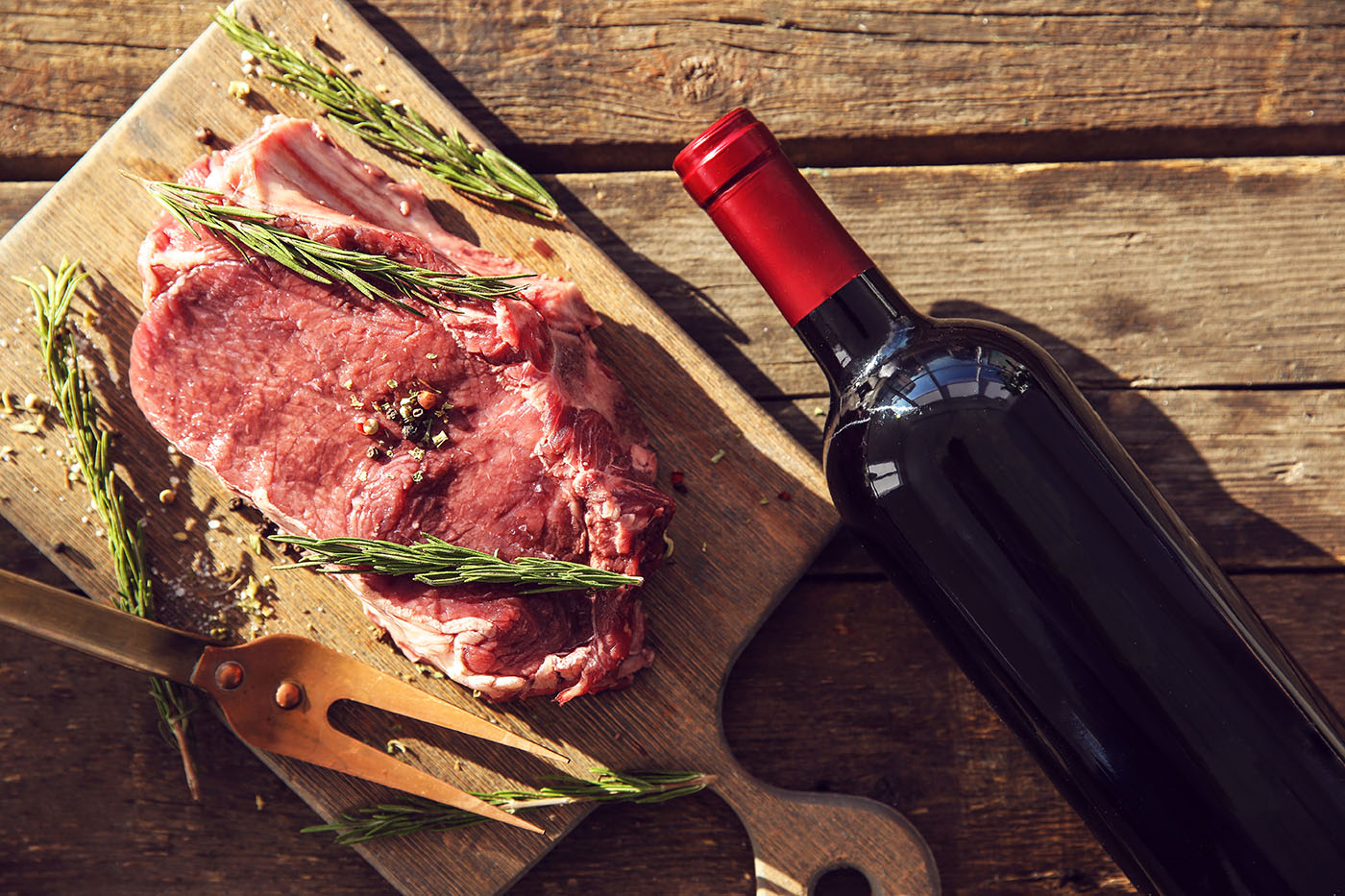 Raw pork steak with bottle of red wine, meat fork and rosemary o